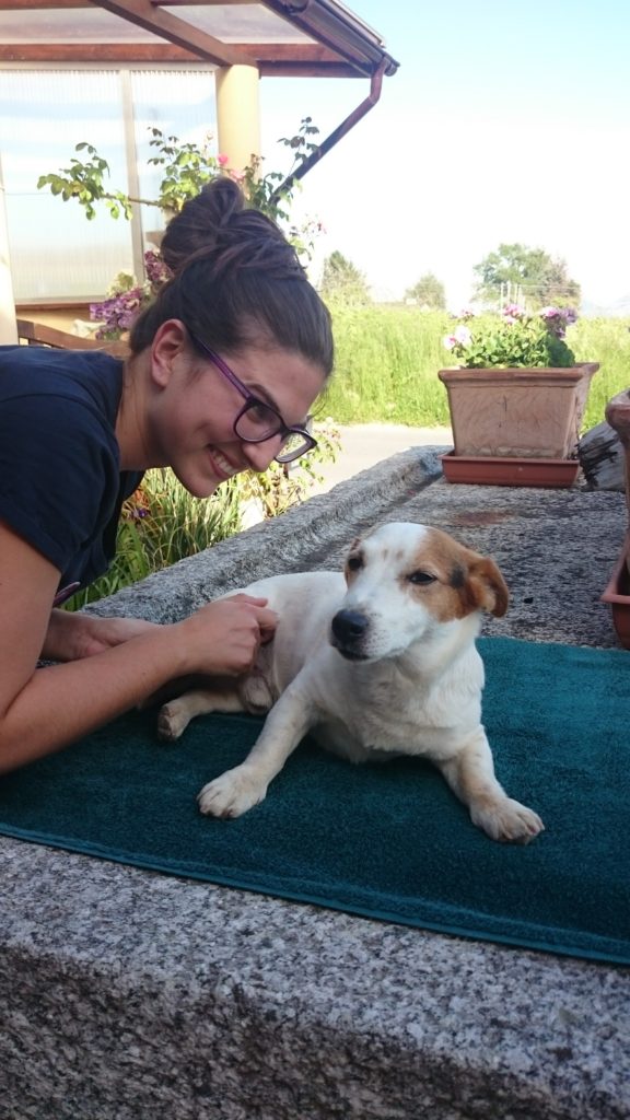 Malika Bolle, co-directrice, souriante, la main posée sur un petit chien blanc et roux allongé sur une serviette