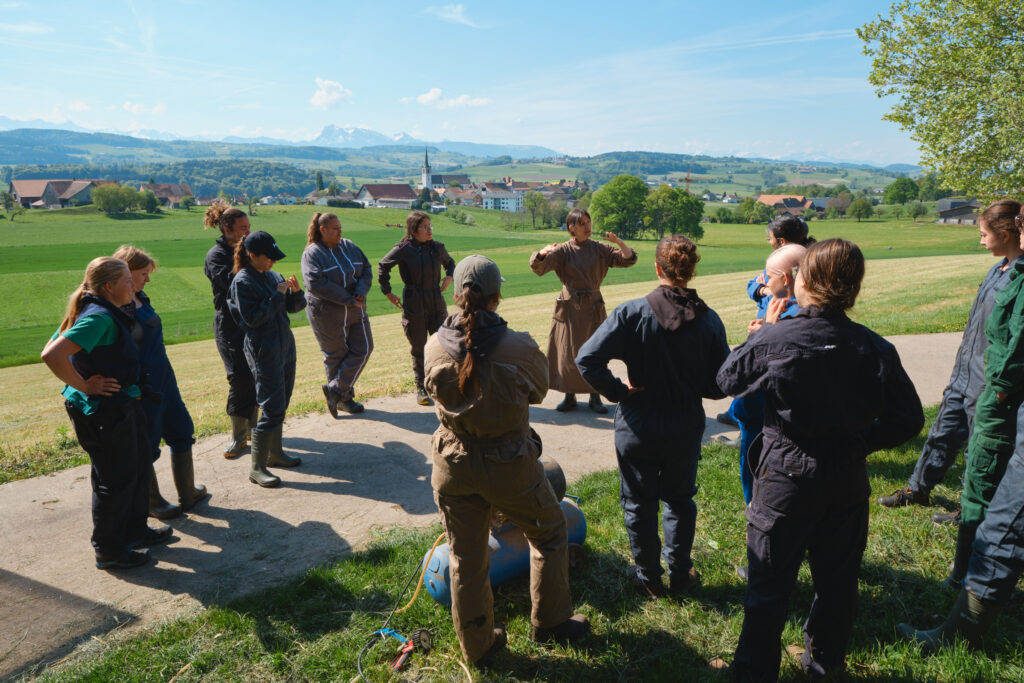 Étudiants en combinaison réunis en cercle autour d'une formatrice, en plein air face aux montagnes