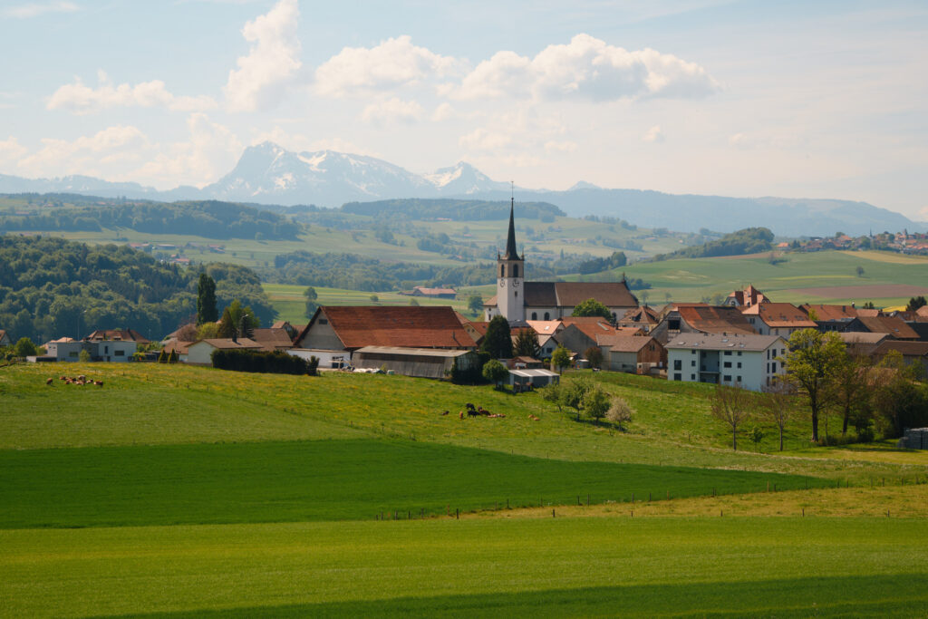 Village et son église au milieu des prés verts, montagnes enneigées à l'horizon