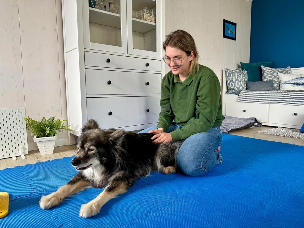 Ana Ceppi, enseignante permanente, agenouillée sur un tapis, la main sur le dos d'un chien à poil long